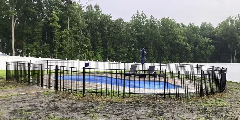 A black aluminum fence surrounding an outdoor in-ground pool. First Step Fence can build a pool fence that protects your property and maintains compliance with Virginia pool fence laws.