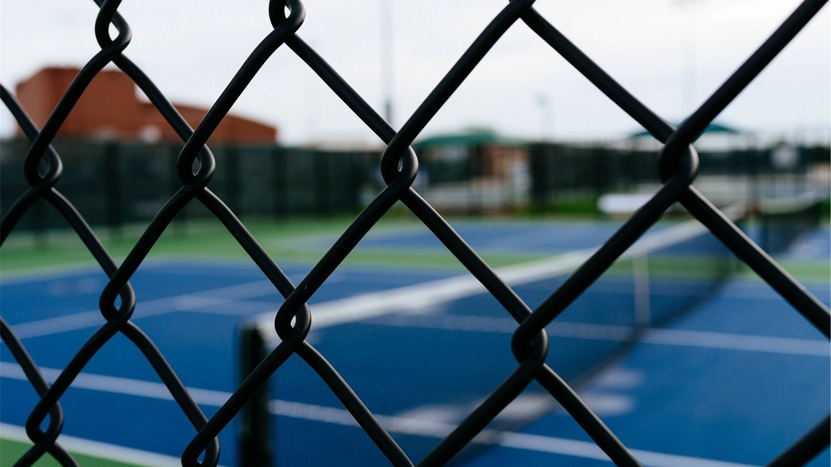 A close-up of a black chain link fence enclosing a tennis court on a commercial property. First Step Fence provides durable and cost-effective commercial chain link fencing solutions for security and functionality in Richmond, Virginia, and the surrounding areas.