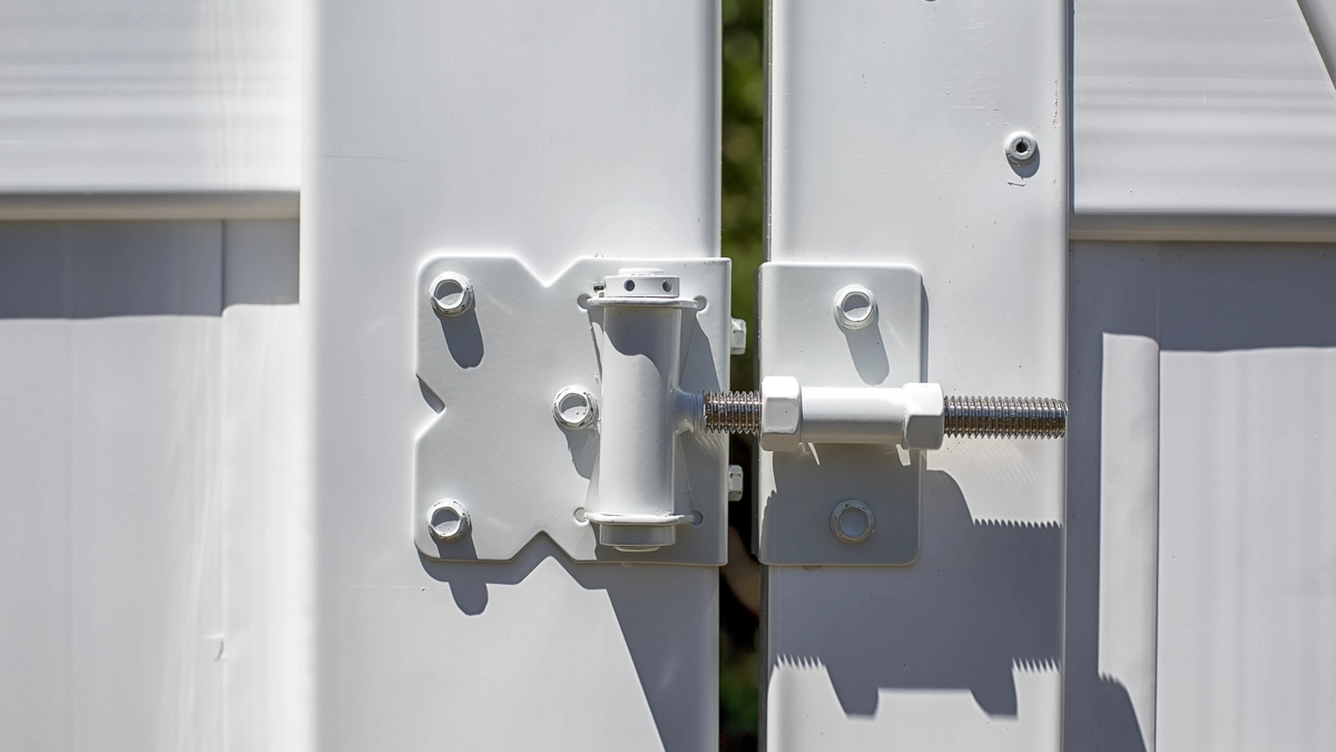 A close-up of a secure white vinyl fence gate hinge and latch, showcasing the durability and craftsmanship of commercial vinyl fencing. First Step Fence provides low-maintenance and professional vinyl fencing solutions for businesses in Richmond, Virginia, and the surrounding areas.