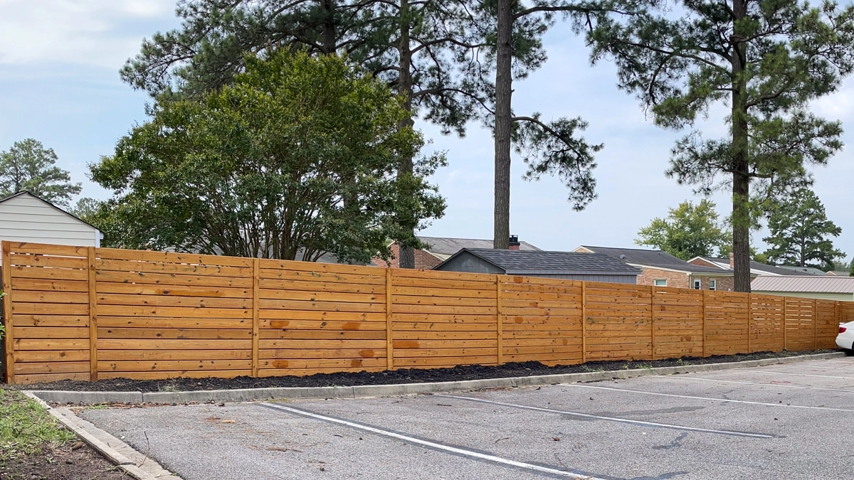 A wood fence enclosing a parking lot. First Step Fence provides custom commercial wood fencing solutions for businesses in Richmond, Virginia, and surrounding areas.