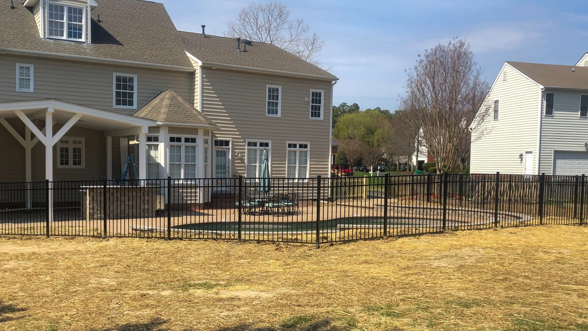 A black aluminum fence enclosing a backyard patio and pool area of a large residential property. First Step Fence offers custom residential aluminum fencing solutions for security, style, and durability in Richmond, Virginia, and the surrounding areas.