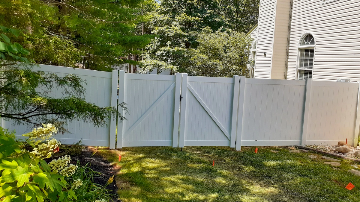 A white vinyl privacy fence with a gate, enclosing a backyard surrounded by lush landscaping and a residential home. First Step Fence provides custom residential vinyl fencing solutions for privacy, durability, and style in Richmond, Virginia, and the surrounding areas.