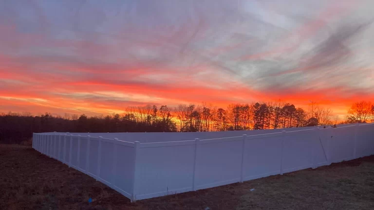 A white vinyl privacy fence enclosing a backyard at sunset, with a vibrant orange and pink sky in the background. First Step Fence provides professional vinyl fencing solutions to Richmond, Virginia, and surrounding areas, delivering quality and customer satisfaction.