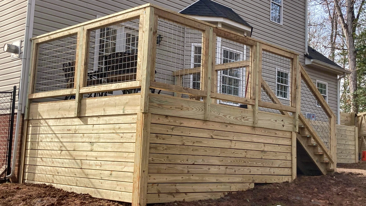 A freshly constructed wood deck in the backyard of a single-family home. The deck railing is made of a combination of wood and wire. First Step Fence offers custom deck installation to the Richmond Virginia area.