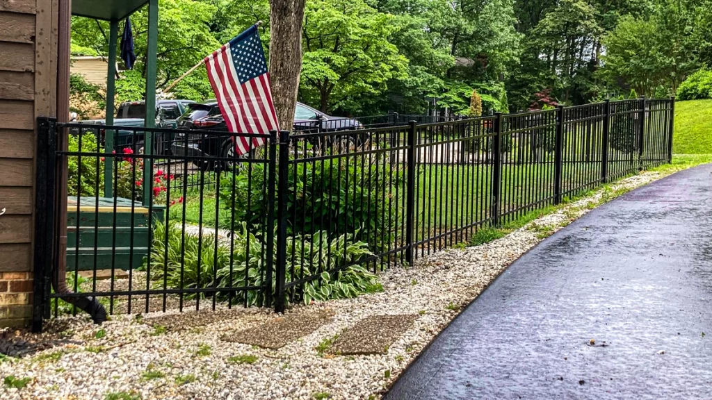 A black residential aluminum fence along a driveway. First Step Fence aluminum fences offer exceptional durability and strength.