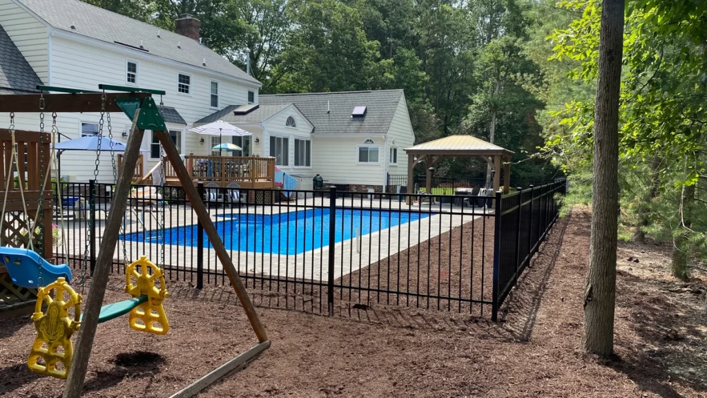 A black aluminum fence enclosing a pool area. First Step Fence aluminum fences are low maintenance and easy to care for.