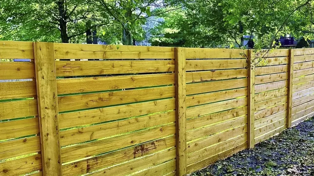 A modern horizontal wooden fence with clean lines, blending seamlessly with its green surroundings. First Step Fence installs sleek, contemporary wood fences.