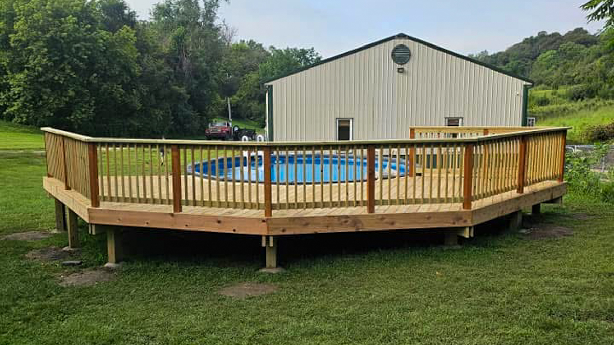 A custom-built wood deck surrounding a pool, showcasing a unique design. First Step Fence offers fully customizable wood decks for your outdoor needs.