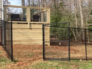 A 6 foot tall black chain link fence, and a pine wood deck using hog wire panels.