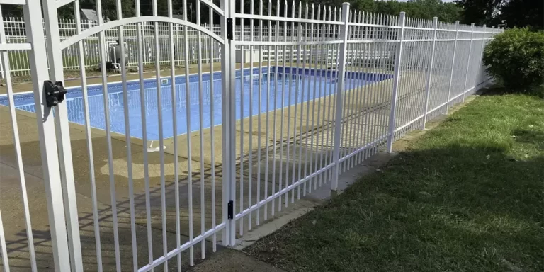 A white aluminum fence surrounding an outdoor, in-ground pool. First Step Fence can help you choose the perfect fence for your home or business.