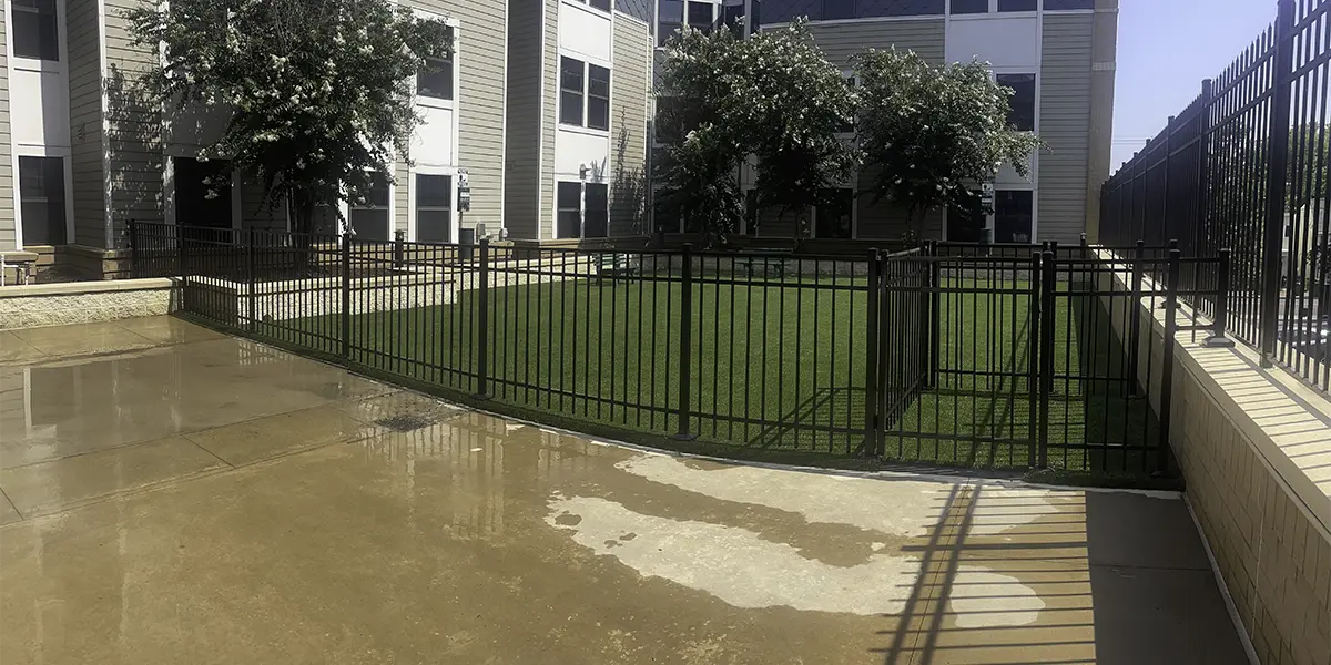 A black aluminum fence surrounding a yard outside of a commercial building. First Step Fence offers professional and reliable commercial aluminum fence solutions to hospitality property, multi-family properties and businesses in Richmond, VA and the surrounding areas.