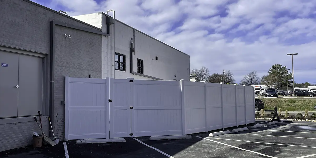 A tall vinyl fence in a commercial building's parking lot. Durable and professional commercial vinyl fencing solutions by First Step Fence for businesses in Richmond, Virginia, and the surrounding areas.