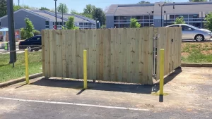 A wood dumpster enclosure with metal posts and parking bollards.