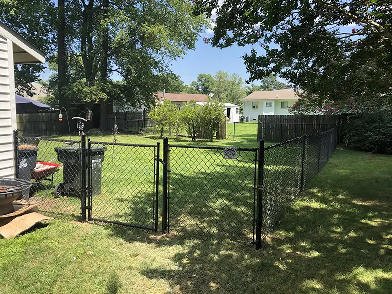 A black, vinyl coated chain link fence with a double gate on a residential property. First Step Fence installs custom gates for chain link fences in Richmond, VA and the surrounding areas.