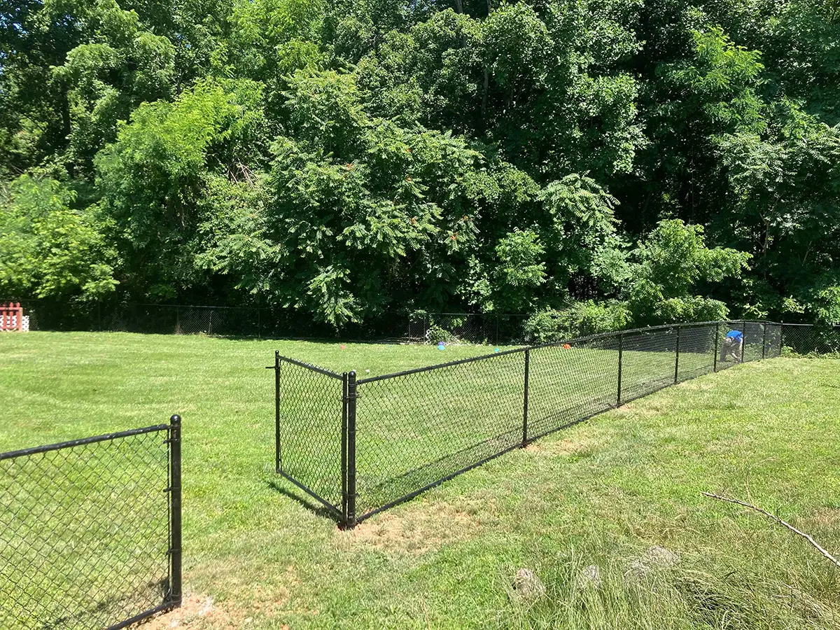 A black chain link fence with an open gate. Durable and practical residential chain link fencing solutions by First Step Fence for secure and functional backyards in Richmond, Virginia.