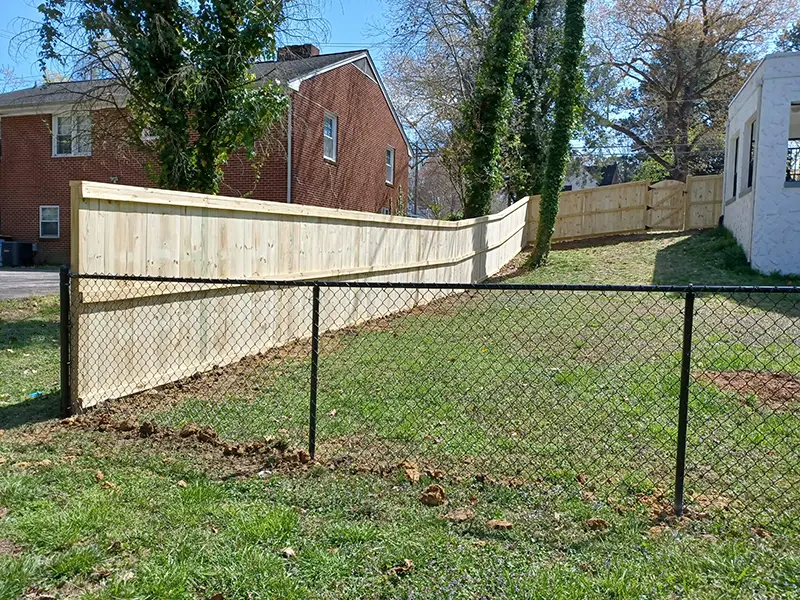 A black, vinyl-coated chain link fence connected to a tall, wood privacy fence on a residential property. First Step Fence offers flexible and versatile fence installations to meet any property's needs.