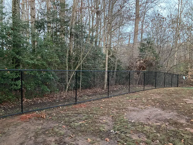 A vinyl coated chain link fence at the property line of a residential yard. First Step Fence offers vinyl coated chain link to residences in Richmond, VA and the surrounding areas.