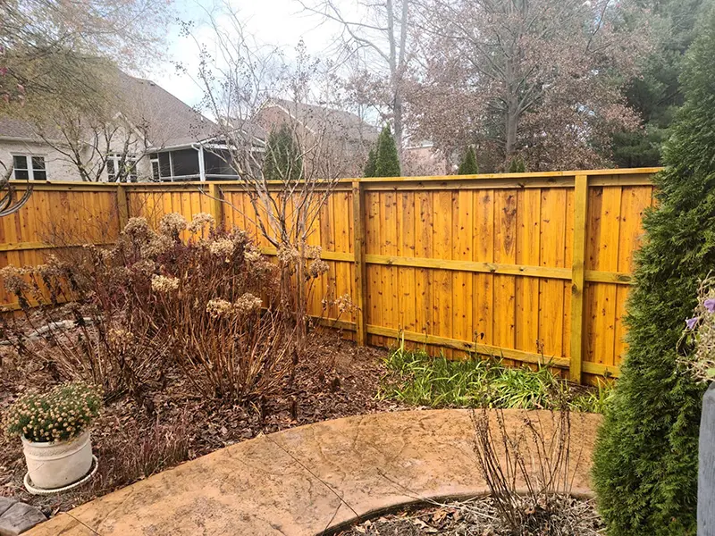 A stained wood fence surrounding a back yard garden. First Step Fence offers exterior wood staining to Richmond, VA and the surrounding areas.