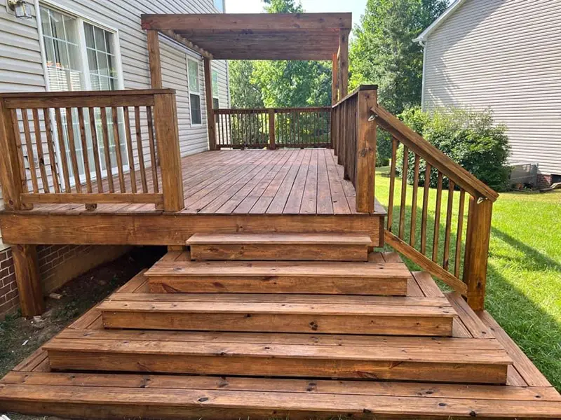 A stained wood deck with a set of stairs and railings. First Step Fence offers exterior wood staining to Richmond, VA and the surrounding areas.