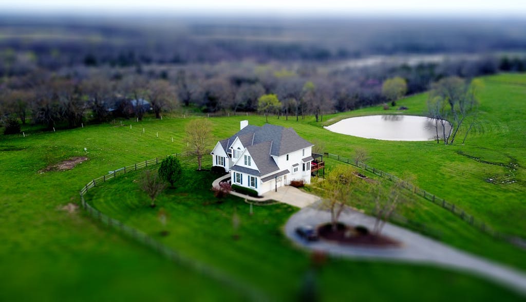 Aerial shot of a charming rural home surrounded by lush green fields and a tranquil pond. Property style, size and terrain will affect your fence options.