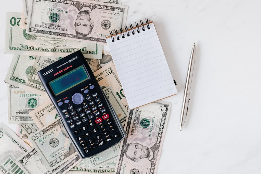 Flat lay of US dollar bills with calculator and notebook for budgeting. When choosing the perfect fence, your budget is a key factor in length, height, materials, and more.