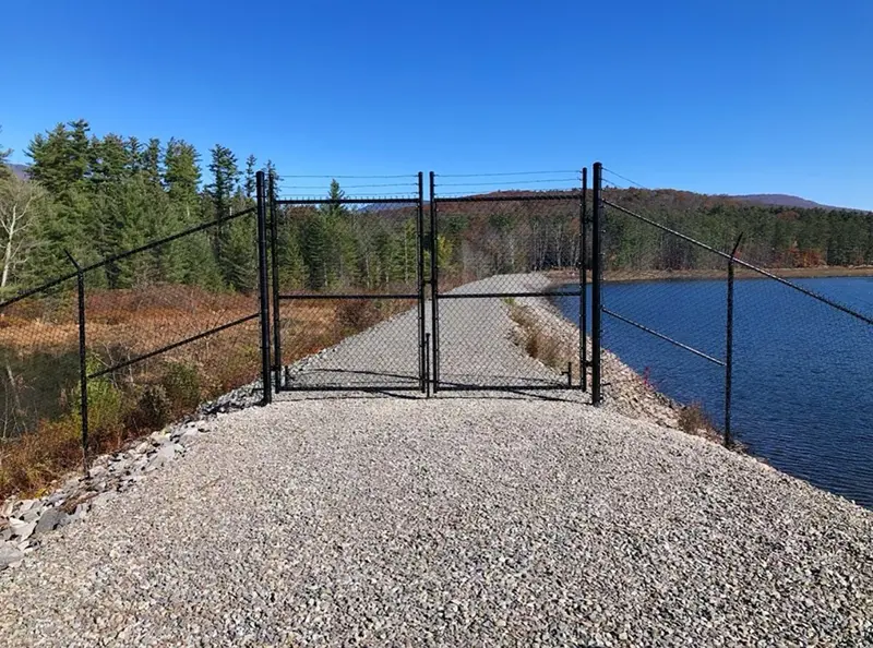 A photograph of a black vinyl chain link fence blocking a gravel path. First Step